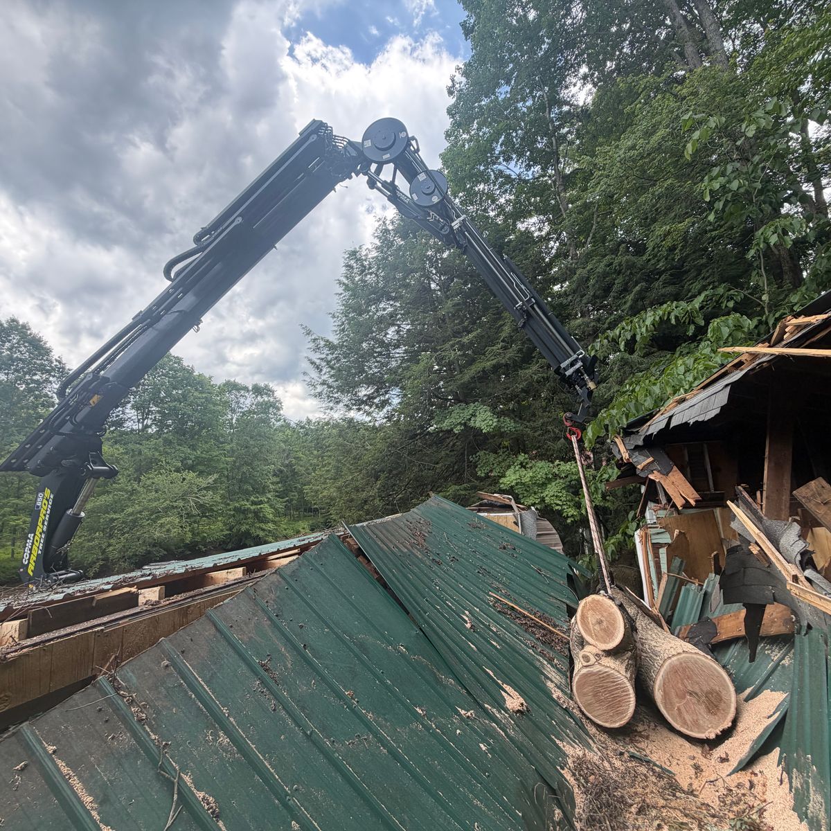 The crane reaching over a barn roof to lift out sectioned logs