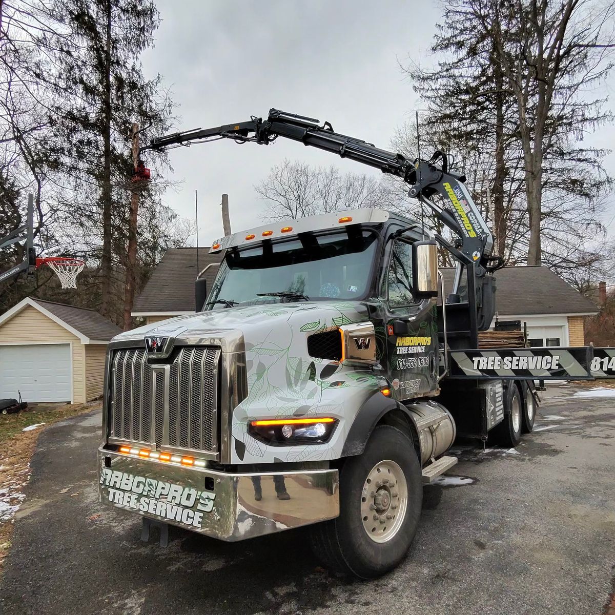 Arbor Pro&rsquo;s crane truck in a winter driveway with the boom raised